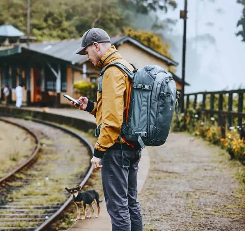A man in a yellow jacket using his phone, standing on a railway track at a hillside station.